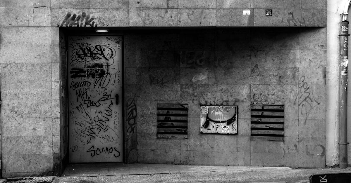 Black and white photograph of a graffiti-covered urban wall in a city setting.