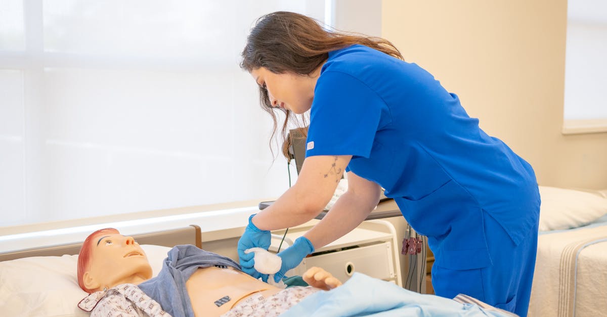 A nurse in blue scrubs practicing medical procedures on a hospital training manikin.
