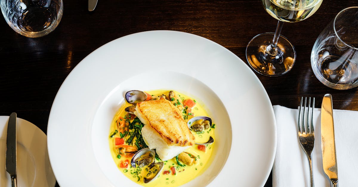 Exquisite seafood dish with clams and fish served at an elegant London restaurant, paired with white wine.