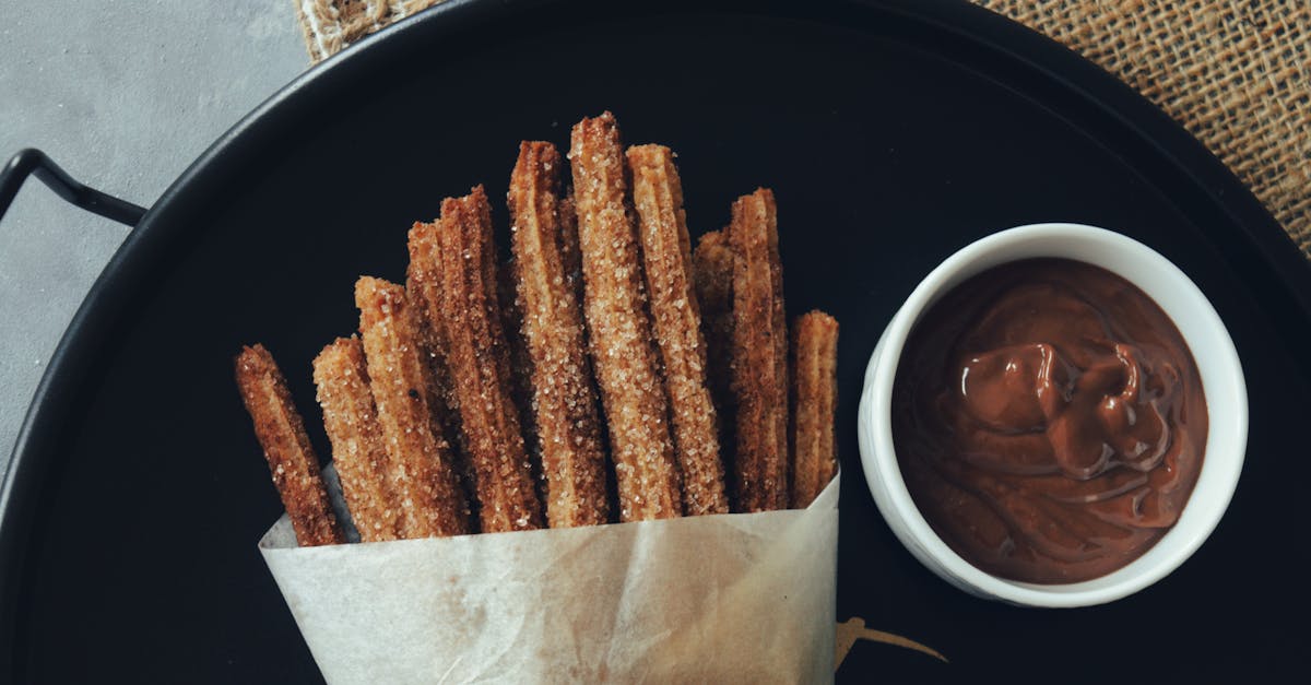 Tray of churros wrapped in paper with a bowl of chocolate sauce on a dark plate.