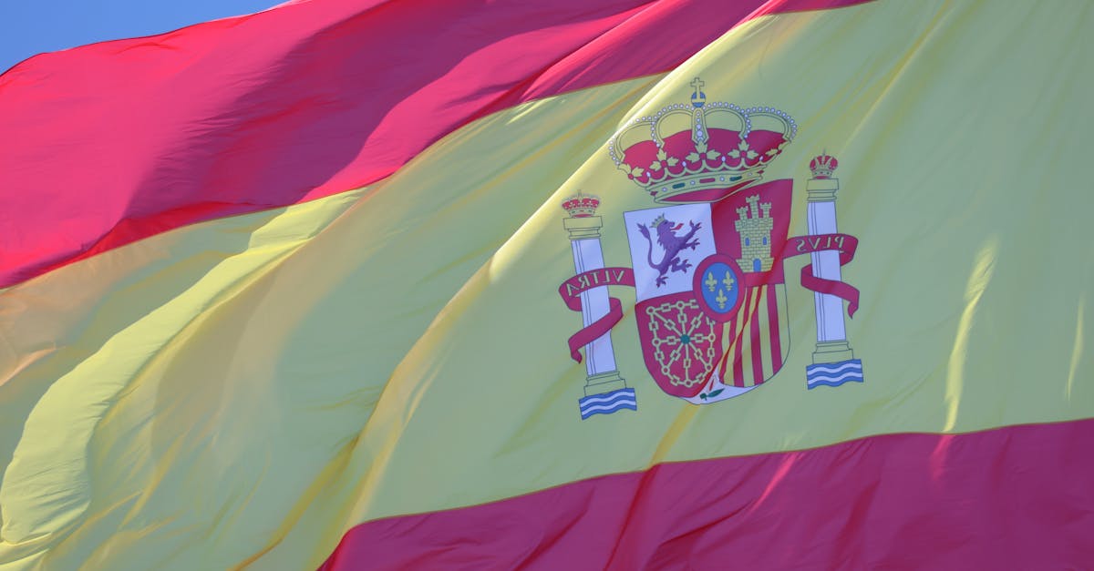 A vibrant Spanish flag with coat of arms waving against a clear blue sky in Cádiz, Andalucía.