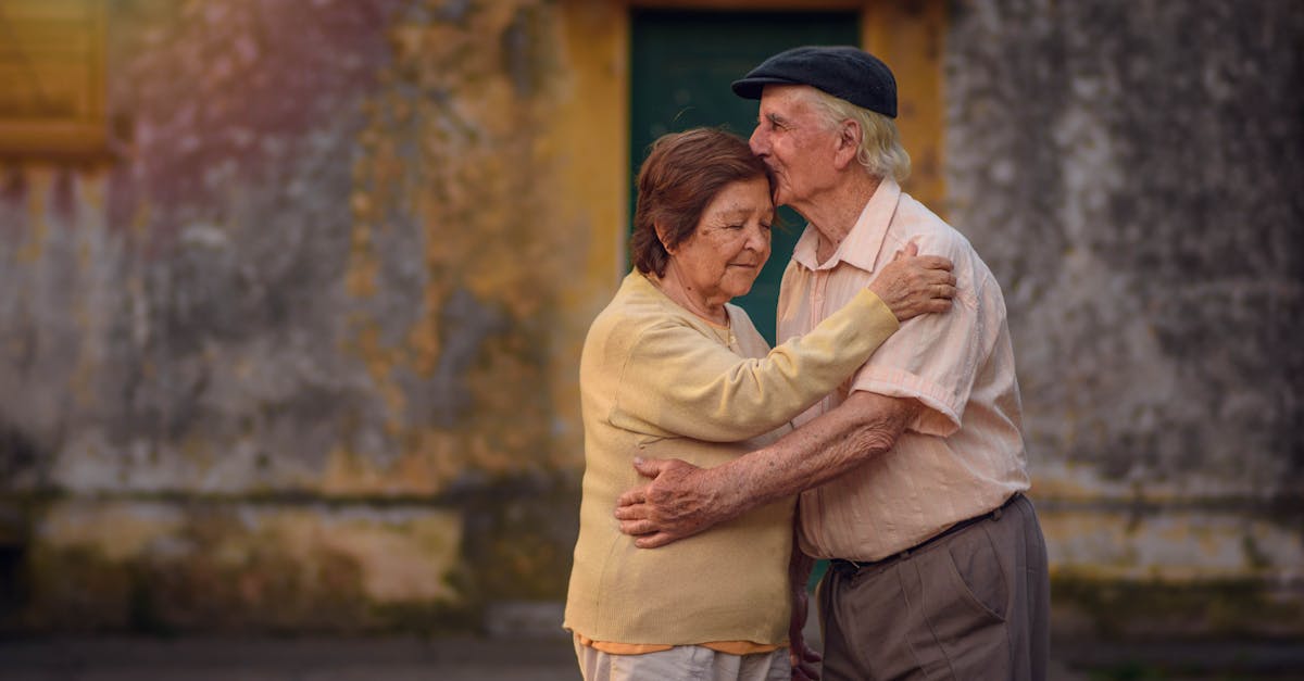 A senior couple sharing a warm embrace outdoors by a weathered wall.