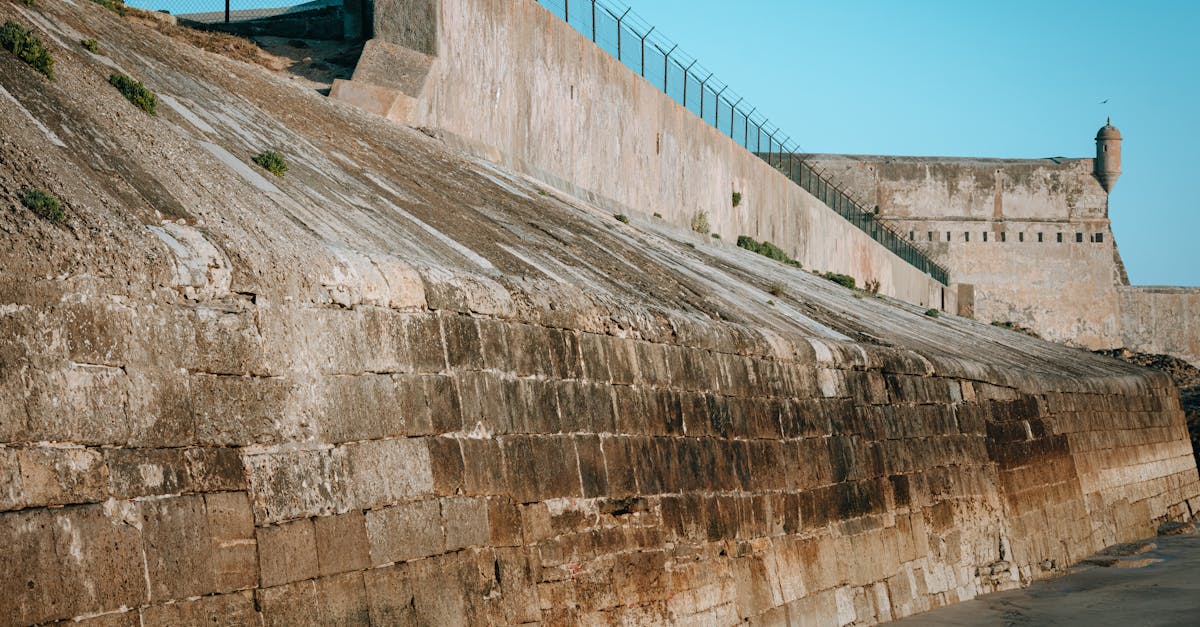 A rugged fortress wall with defensive features under a clear blue sky, showcasing historic architecture.