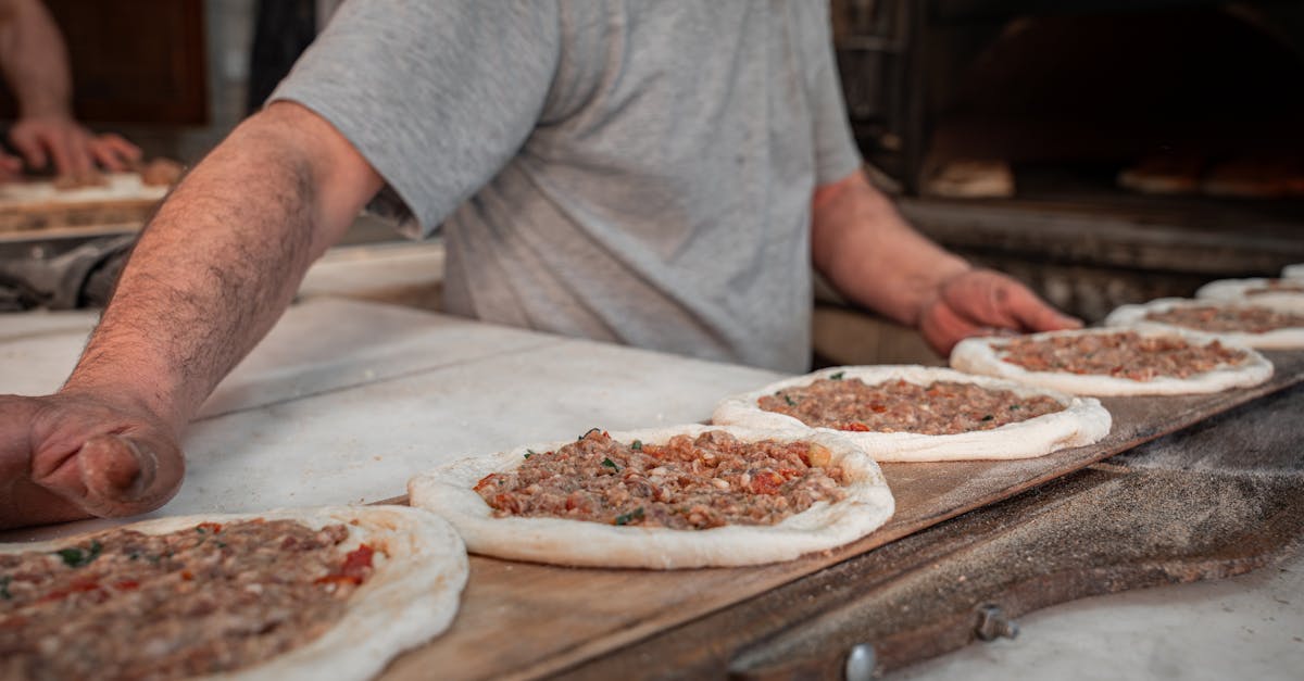 A baker arranging meat-topped flatbreads on a wooden board in a bakery setting.