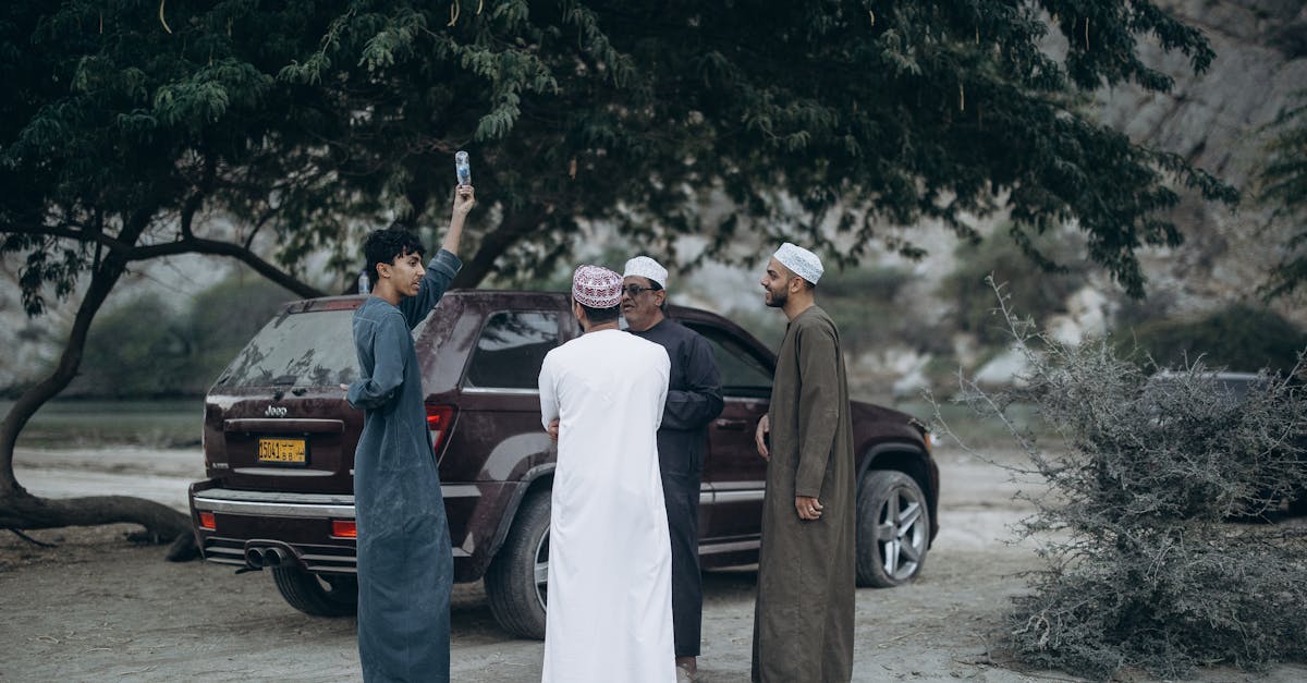 A group of Omani men socializing under a tree by a parked vehicle in Nizwa, Oman.