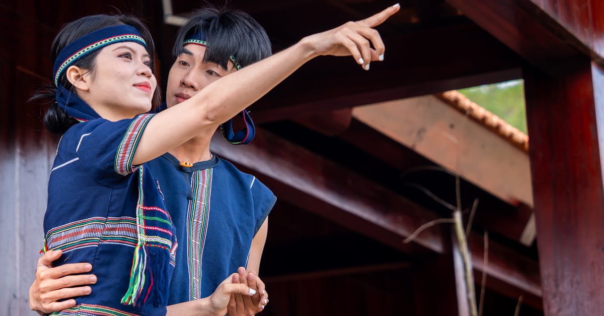 A couple in traditional attire pointing while standing outdoors under a wooden structure.