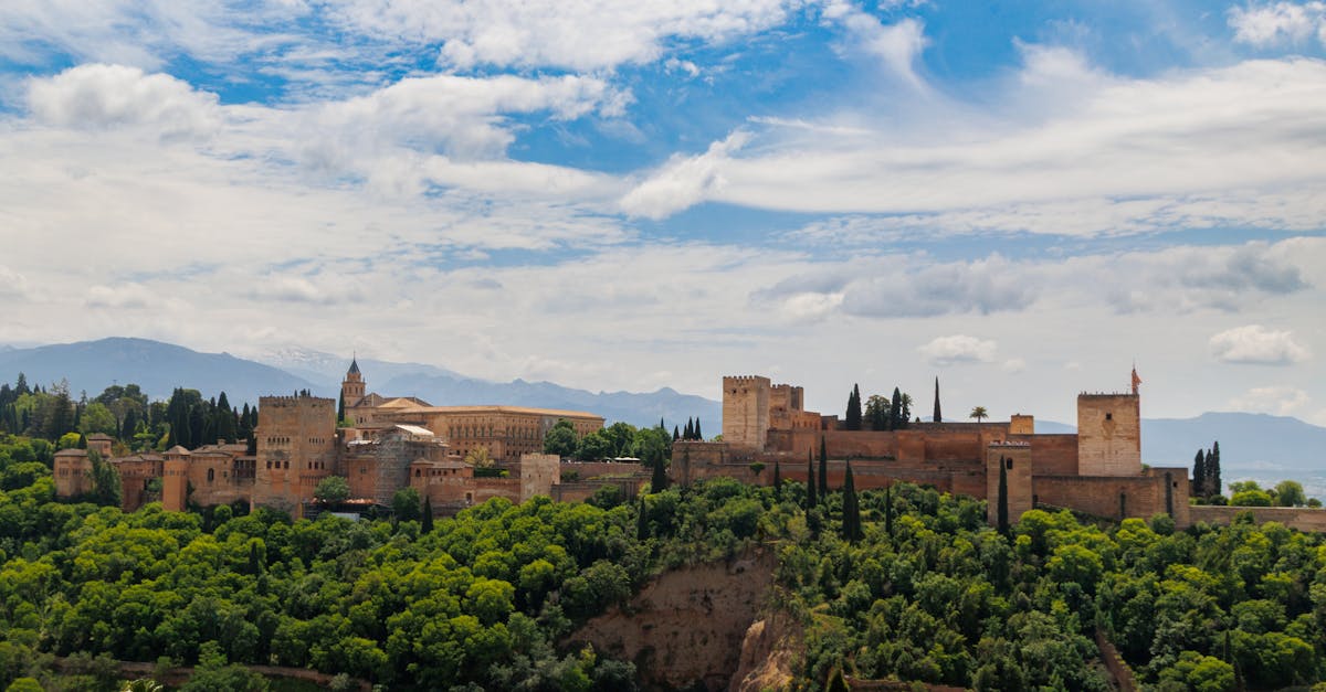 A scenic view of the Alhambra Palace surrounded by greenery under a vibrant blue sky in Granada, Spain.