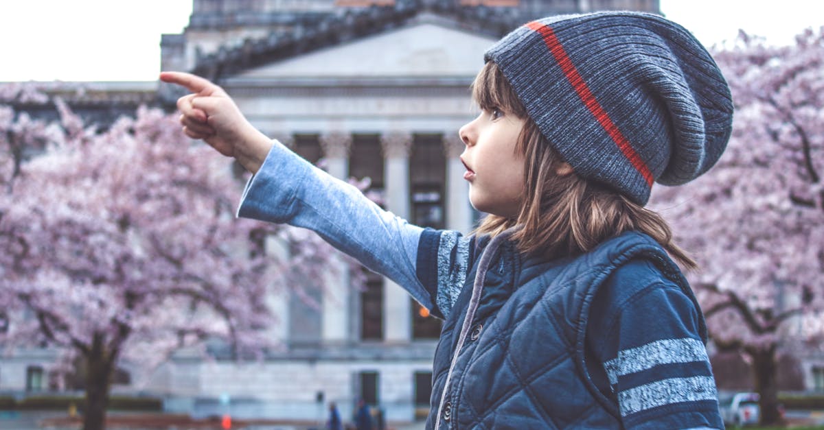 A young girl in a beanie points towards cherry blossoms in front of a historic building.