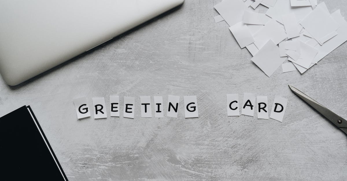 Top view of greeting card arrangement with paper, scissors, and laptop on a gray surface.