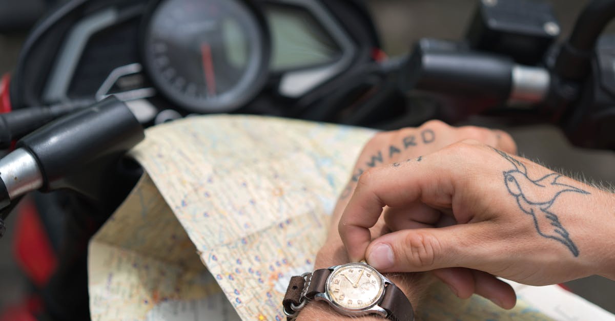 From above of crop anonymous tattooed male configuring watch sitting on motorcycle with city map