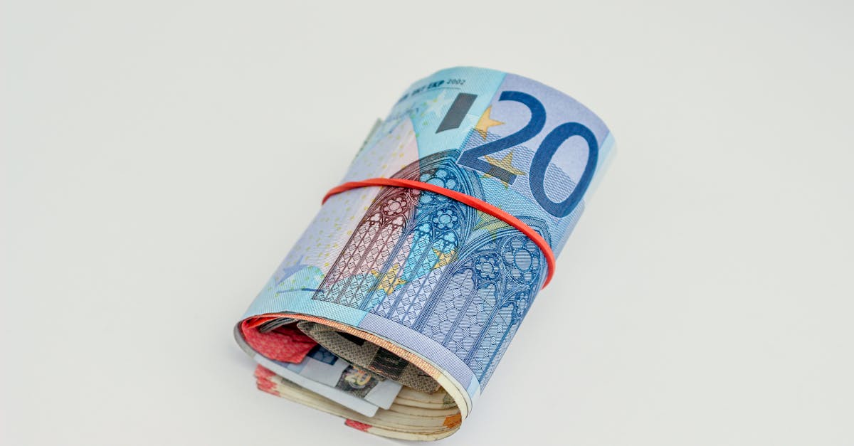 Close-up of rolled euro banknotes secured with a red rubber band on white background.
