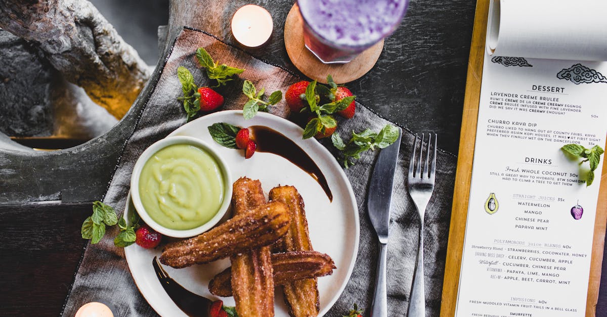 From above of delicious Spanish churros with green dip sauce garnished with fresh strawberries and melted chocolate near glass of blueberry milkshake and menu in restaurant