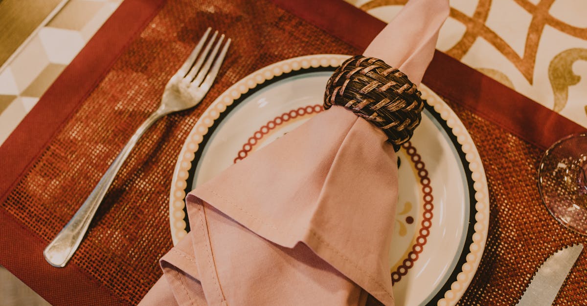 From above layout of table setting with pink napkin served on fancy ceramic plate on place mat near cutlery