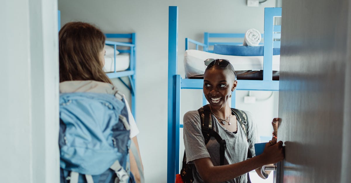 Two women backpackers entering a hostel dorm room with bunk beds, smiling and excited for their adventure.