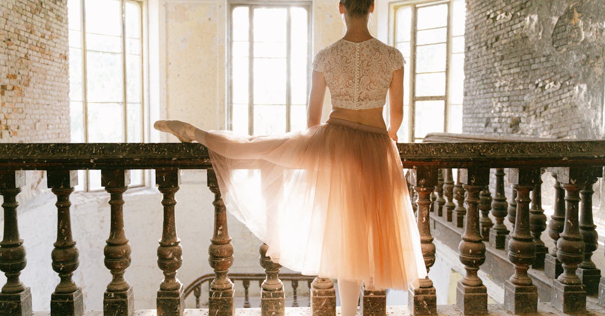 A graceful ballerina stretches indoors against a vintage railing, lit by soft sunlight.