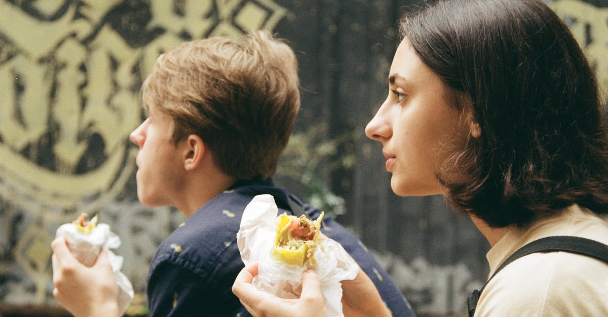 Two young adults savoring sandwiches outdoors, depicting a casual urban scene.