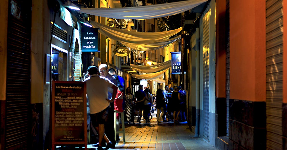 Lively city alley at night with people gathering in a bustling, illuminated atmosphere.