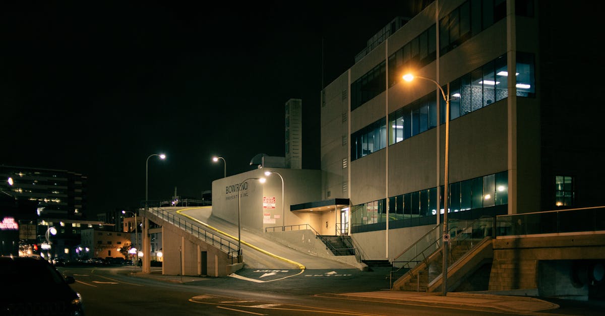 Empty asphalt roadway with marking lines near modern building and luminous streetlamps at night
