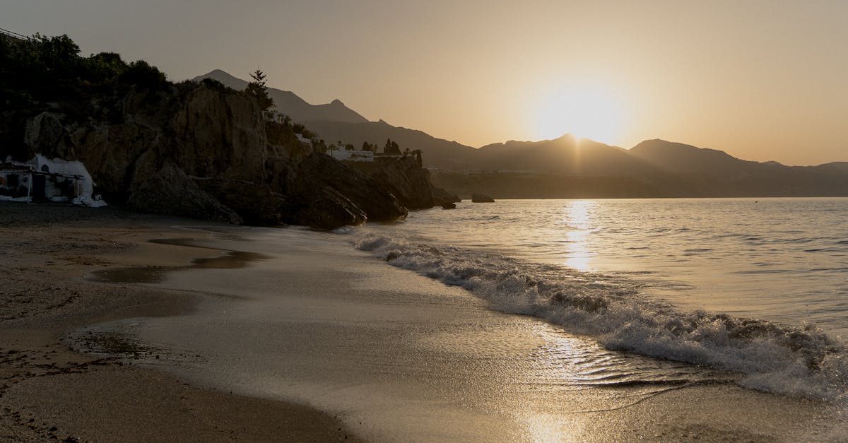 A peaceful sunset on a sandy beach with waves and impressive rocky cliffs in view.