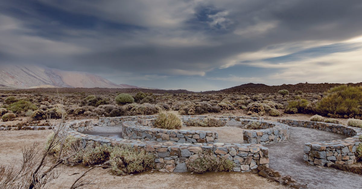 A circular stone structure surrounded by a serene desert landscape under a dramatic cloudy sky.