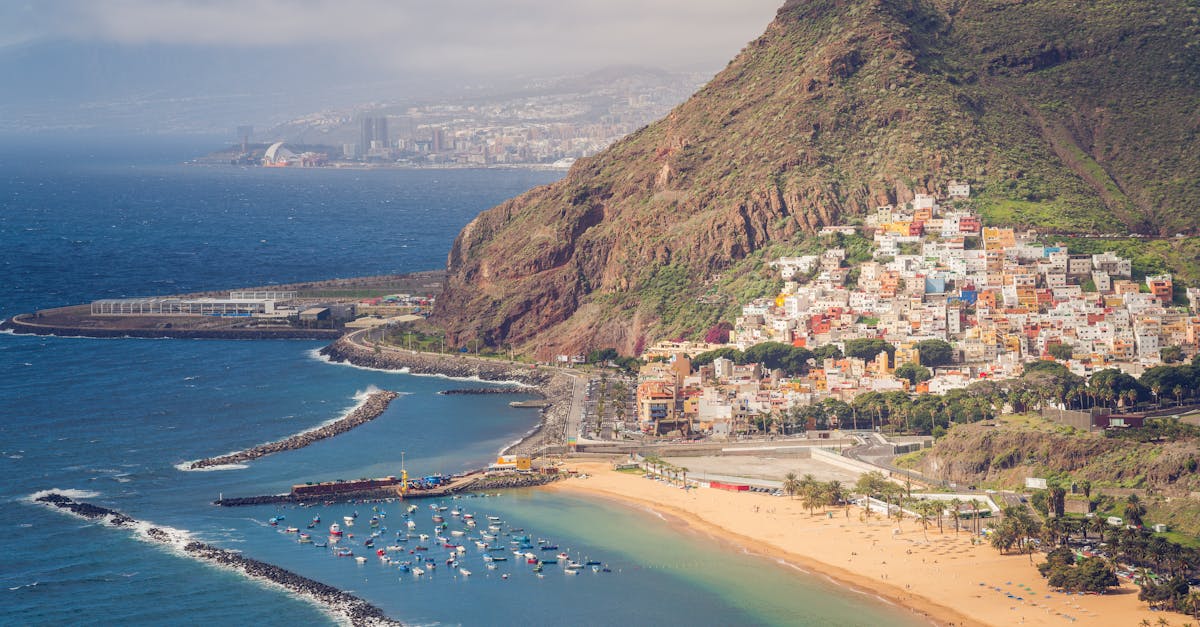 Scenic aerial view of a coastal city with lush mountains, a golden sandy beach, and blue ocean.