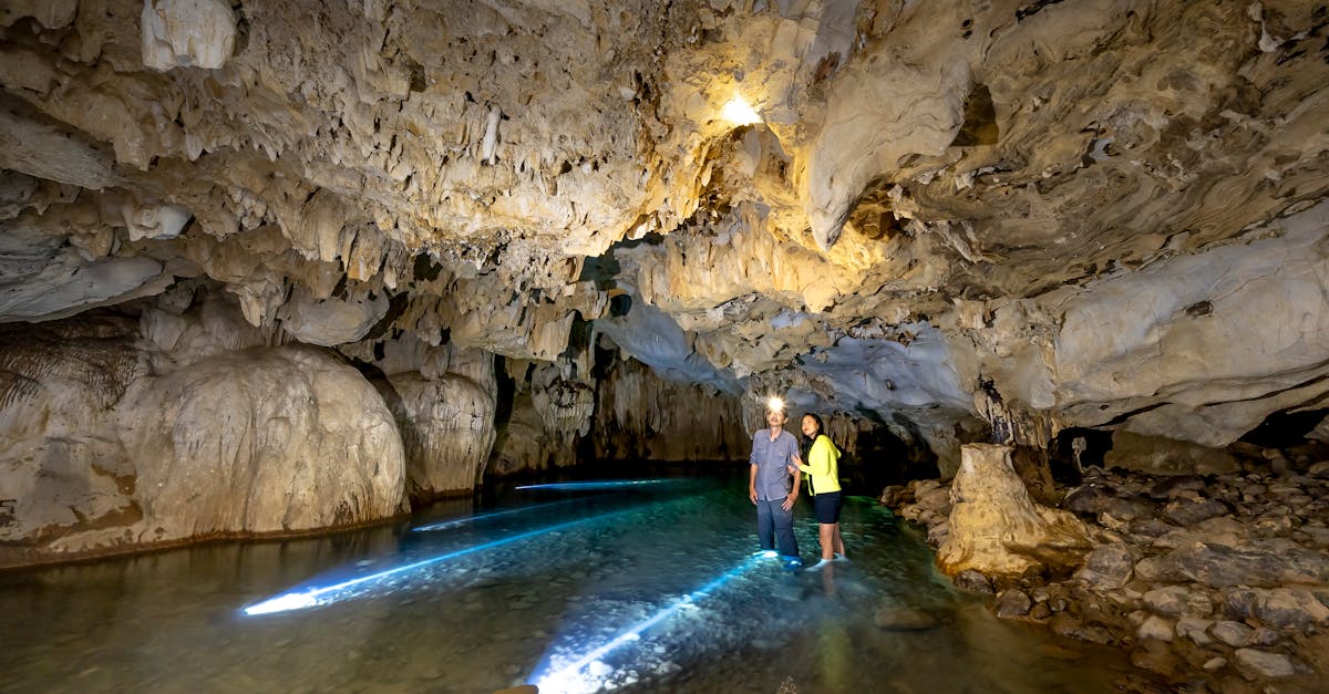 Two people exploring a beautifully illuminated underground cave with water reflections.