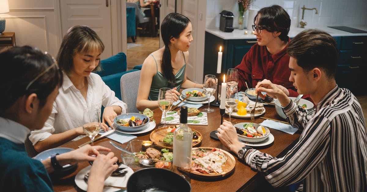 A diverse group of friends sharing dinner at a cozy dining table with wine and lighted candles.