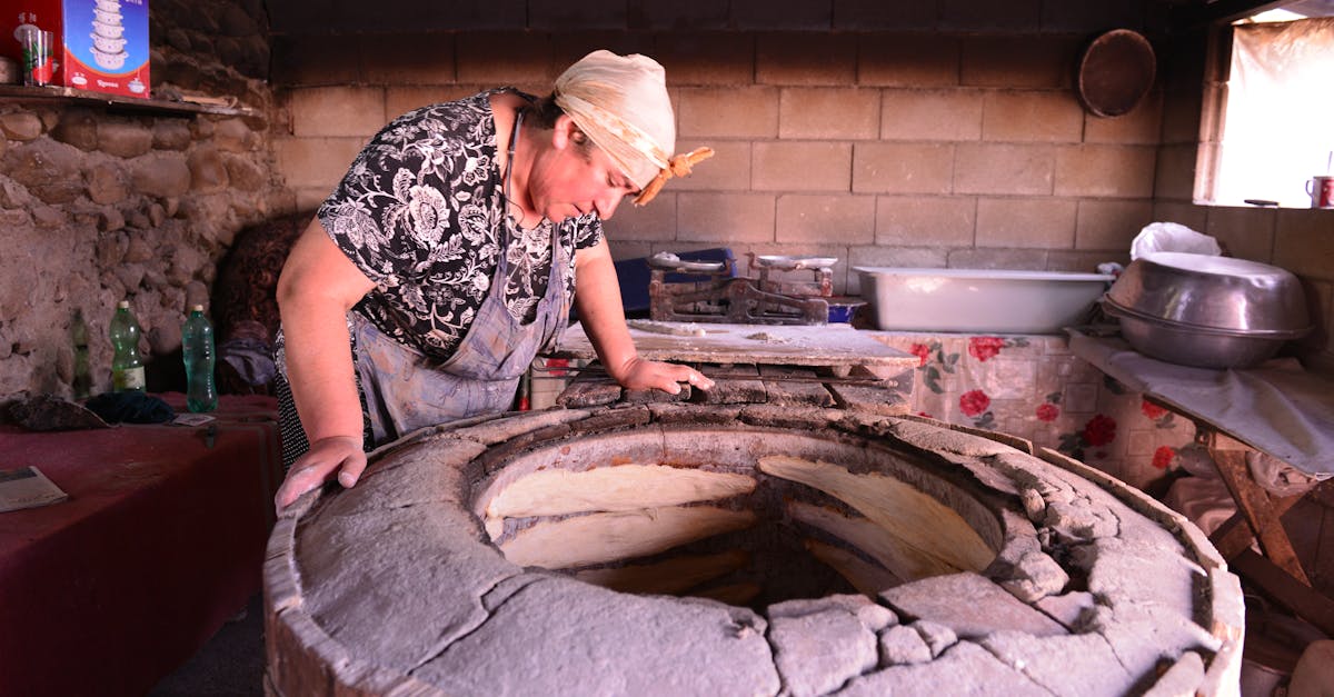 A woman bakes bread in a traditional stone oven in a rustic kitchen setting.
