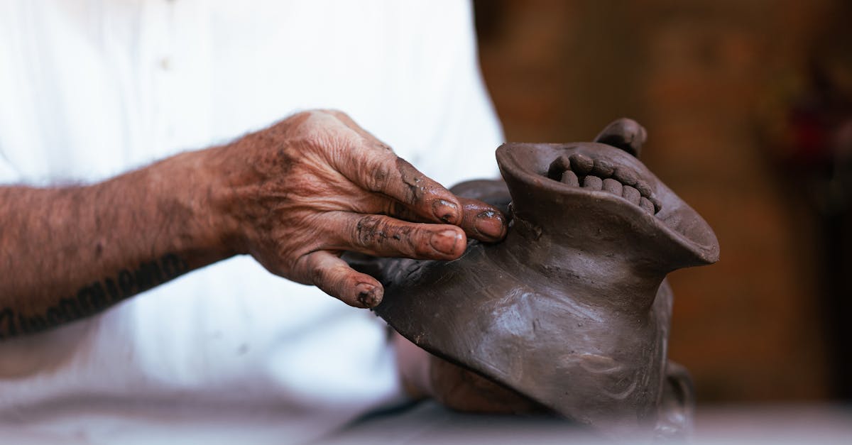 Close-up of a skilled artisan crafting a clay mask with precise hand movements in a workshop.
