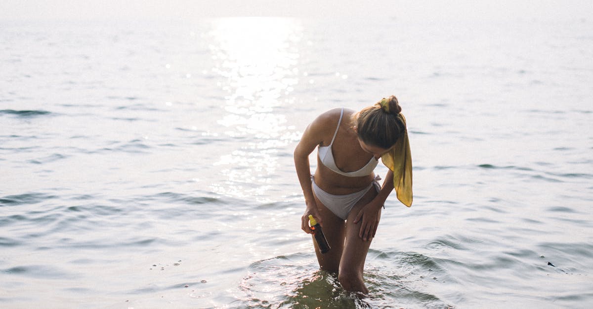 A woman in a bikini applying sunscreen at the beach during sunset, capturing a serene summer moment.