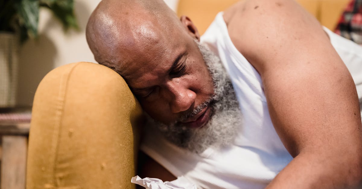 A bearded man sleeps on a couch, appearing tired in a cozy indoor setting.
