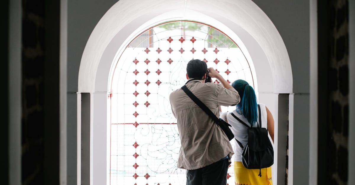 A couple takes photos through an arched stained glass window, showcasing artistic interior architecture.