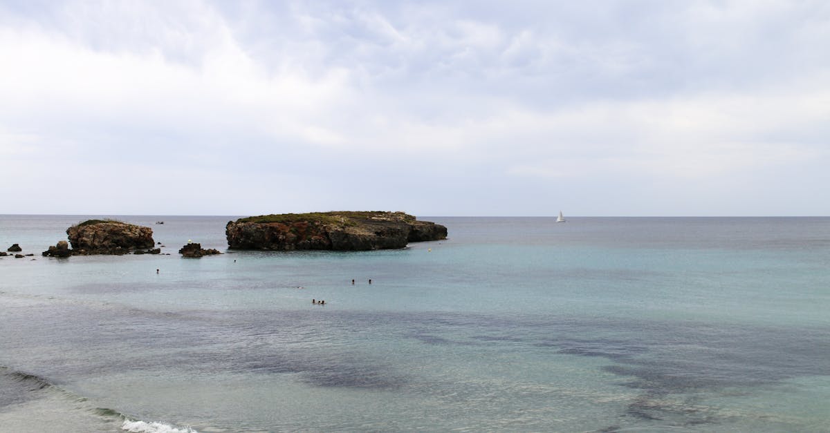 Serene view of the Mediterranean Sea near Ciutadella de Menorca with scattered islets and a distant sailboat.