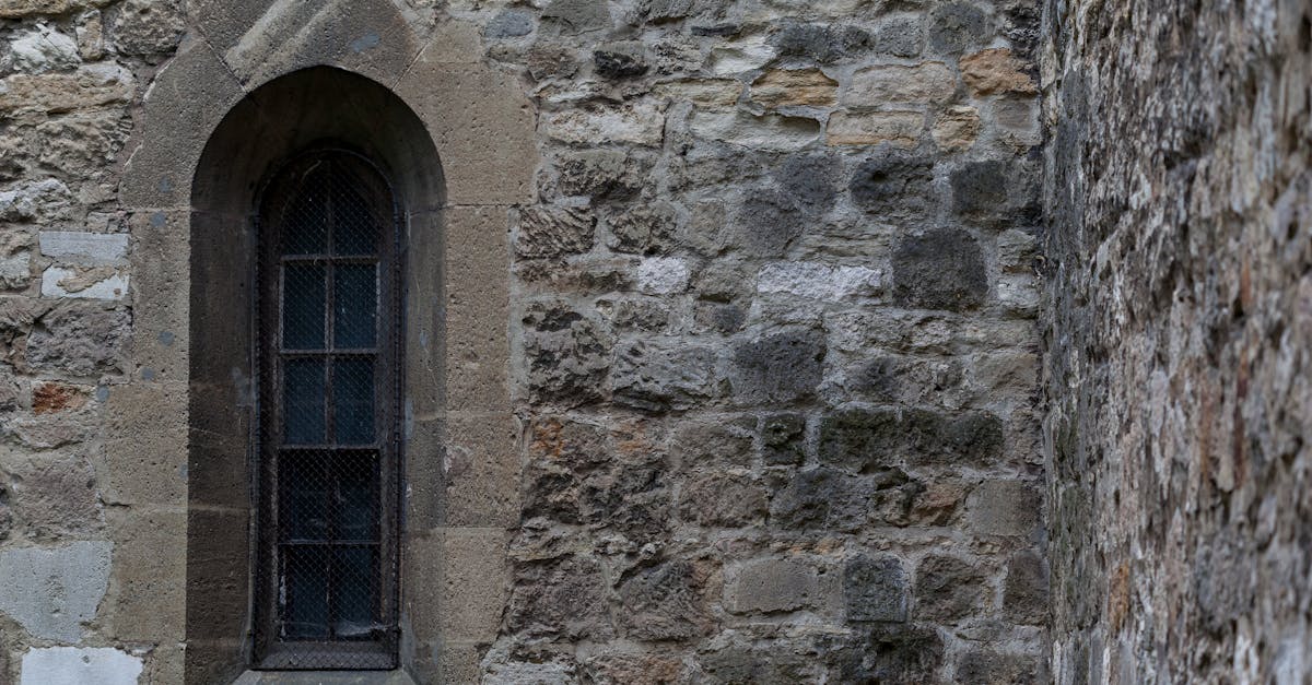 Close-up of an arched window set in a rustic stone wall, showcasing medieval architecture.