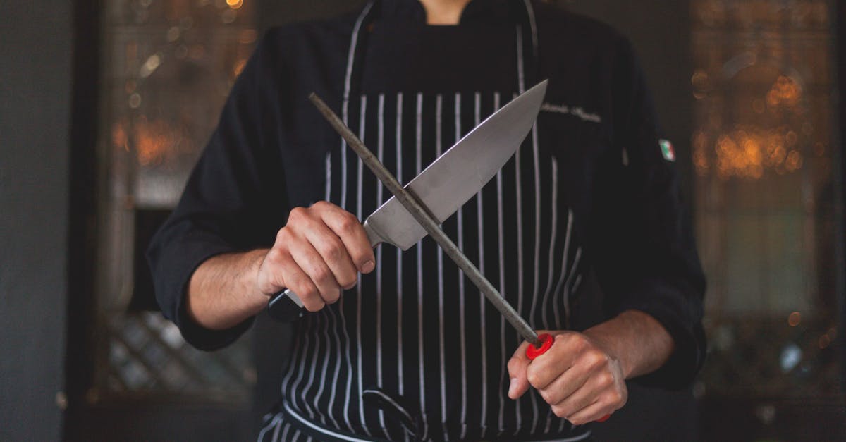 Chef sharpening a knife with a honing rod in a professional kitchen setting, focusing on precision and culinary skill.