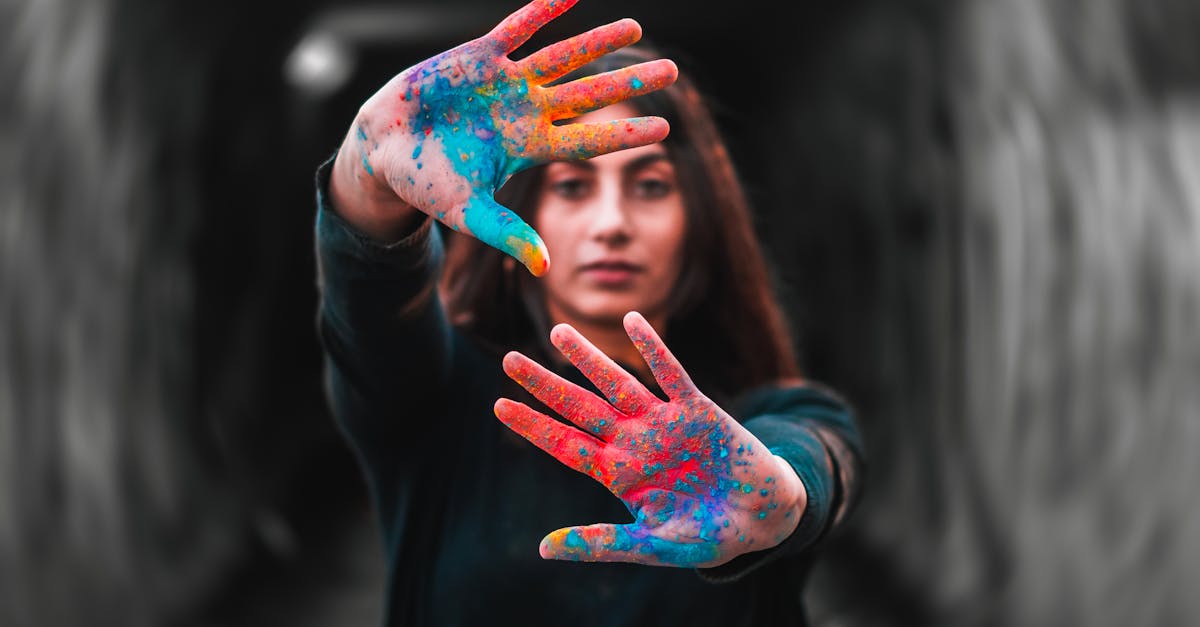 A woman showcasing colorful painted hands, focusing on vibrant creativity in a blurred background.