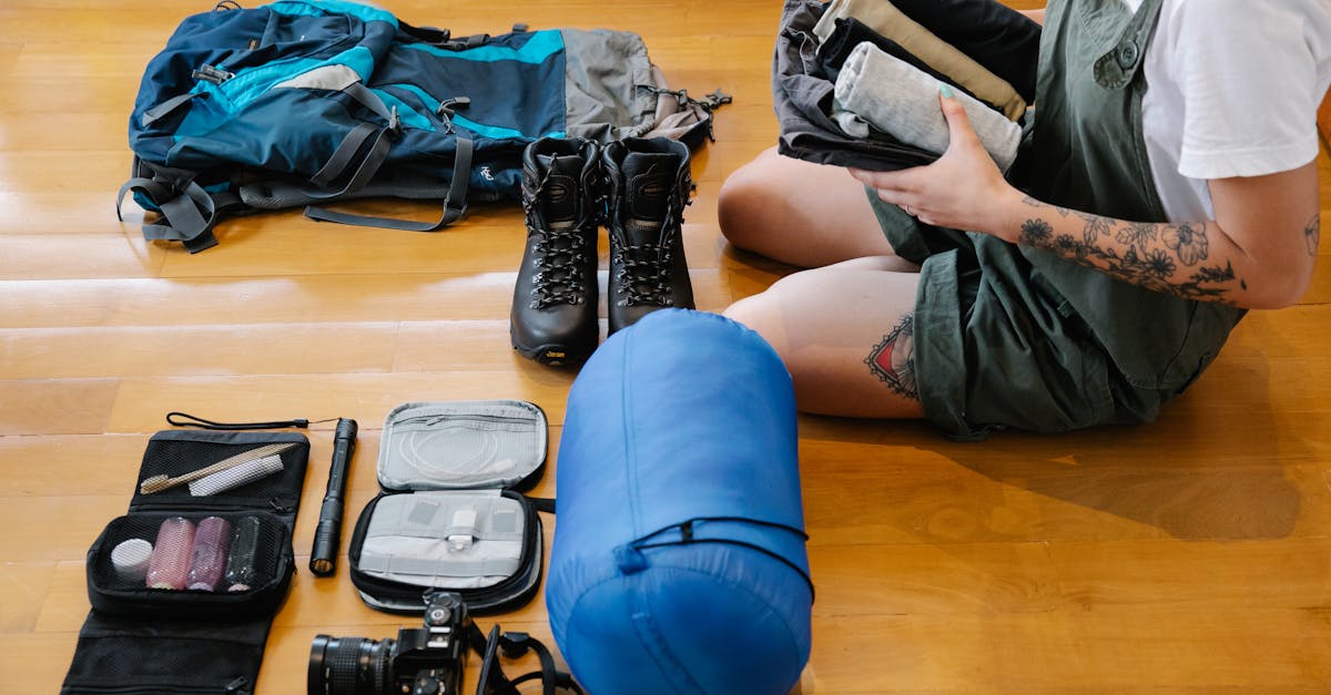 Woman organizing camping gear and clothes on wooden floor indoors, preparing for an adventure.